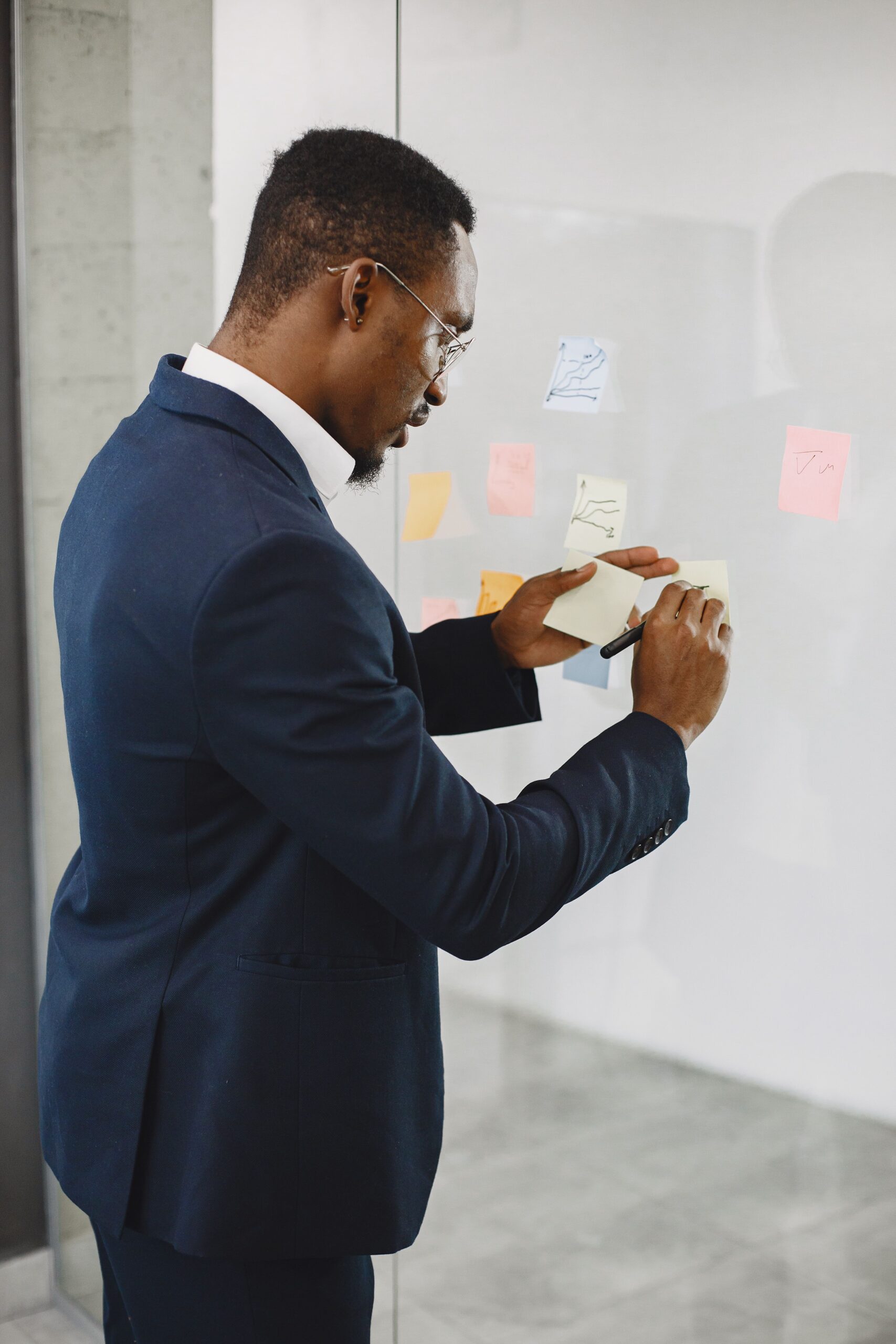 African professional mapping operational feedback loops with sticky notes on a glass wall