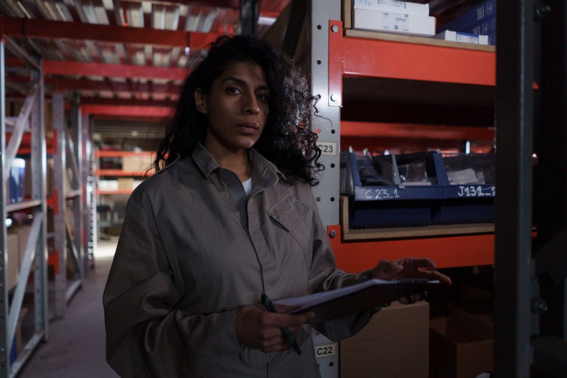 Black woman checking inventory records in a warehouse aisle